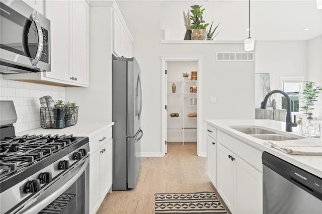 kitchen with appliances with stainless steel finishes, sink, pendant lighting, light hardwood / wood-style flooring, and white cabinets