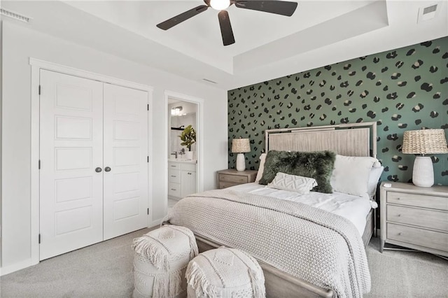 bedroom featuring ensuite bath, light colored carpet, a tray ceiling, ceiling fan, and a closet