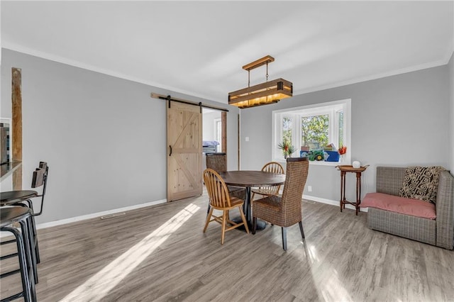 dining room with hardwood / wood-style floors, a barn door, and ornamental molding