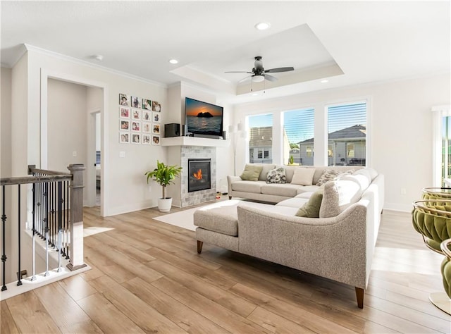 living room with ceiling fan, light hardwood / wood-style floors, a raised ceiling, and ornamental molding