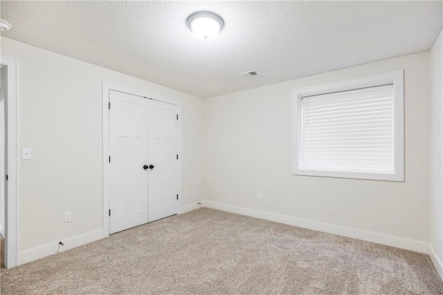 unfurnished bedroom featuring light colored carpet, a textured ceiling, and a closet