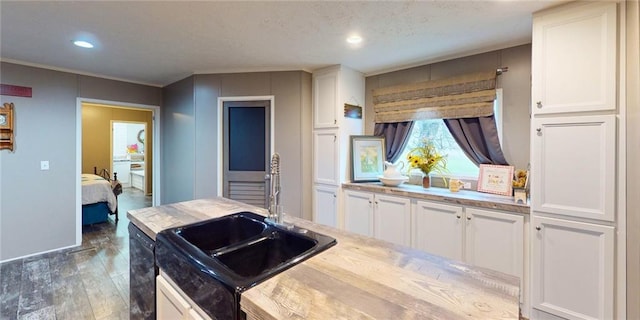 kitchen featuring dark wood-type flooring, sink, a textured ceiling, black dishwasher, and white cabinetry