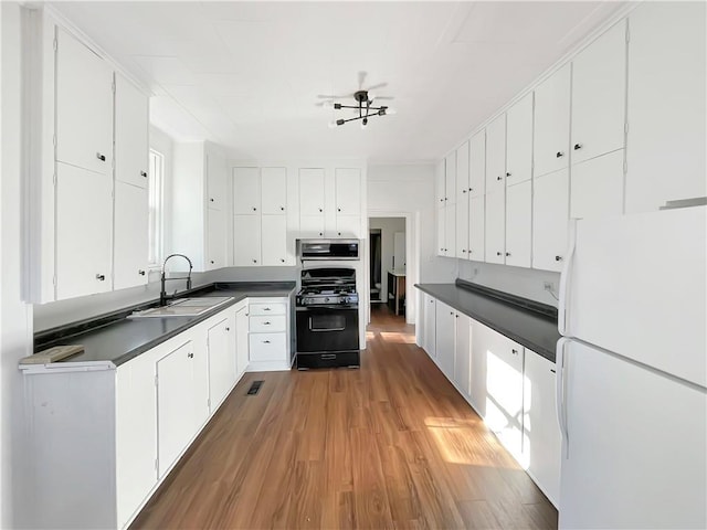 kitchen featuring black range with gas stovetop, sink, wood-type flooring, white fridge, and white cabinetry