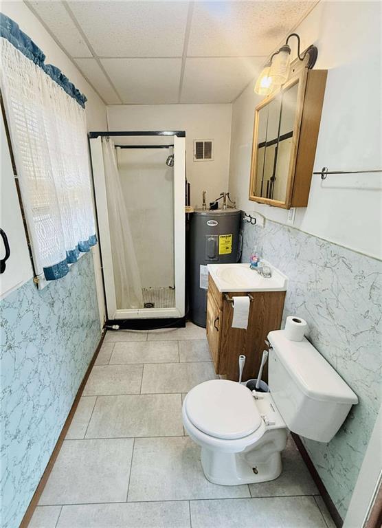 bathroom with a drop ceiling, a shower with curtain, electric water heater, tile walls, and toilet