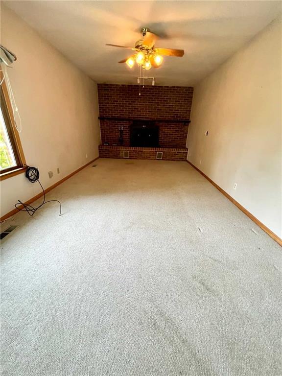 unfurnished living room featuring ceiling fan, carpet, and a brick fireplace