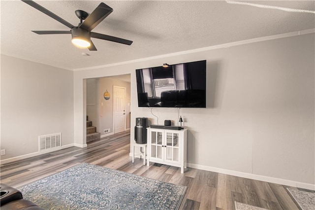 living room featuring ceiling fan, wood-type flooring, a textured ceiling, and ornamental molding