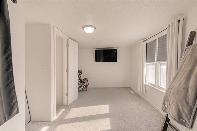 hall with a textured ceiling and light colored carpet