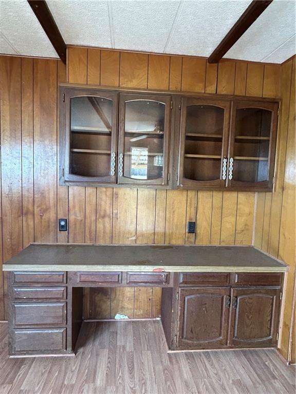 unfurnished office with wood walls, a textured ceiling, and light hardwood / wood-style flooring