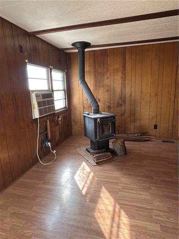 living room with a wood stove, wooden walls, light hardwood / wood-style flooring, and a textured ceiling