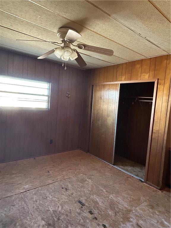 unfurnished bedroom with a closet, wooden walls, and ceiling fan