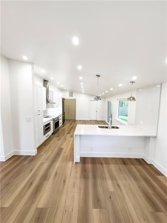 kitchen with white cabinets, light hardwood / wood-style flooring, wall chimney exhaust hood, and decorative light fixtures