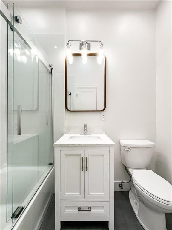 full bathroom with combined bath / shower with glass door, toilet, and vanity