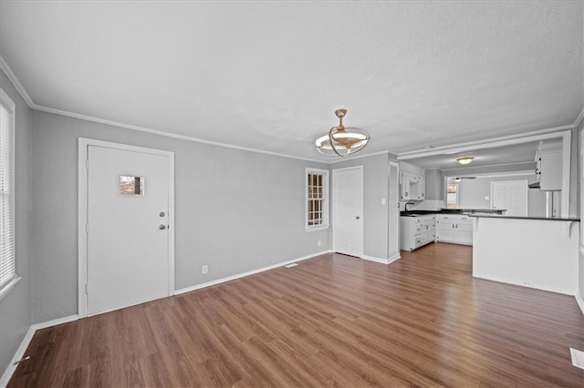 unfurnished living room with crown molding, dark hardwood / wood-style floors, and an inviting chandelier