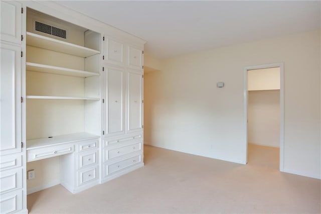 unfurnished bedroom featuring a spacious closet, a closet, built in desk, and light colored carpet