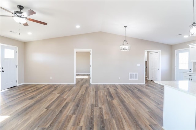 unfurnished living room featuring a healthy amount of sunlight, ceiling fan with notable chandelier, dark wood-type flooring, and lofted ceiling