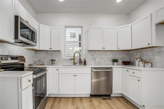 kitchen with appliances with stainless steel finishes, light wood-type flooring, white cabinetry, and sink