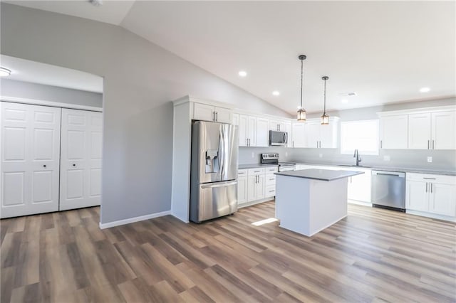 kitchen featuring white cabinets, hanging light fixtures, vaulted ceiling, appliances with stainless steel finishes, and a kitchen island