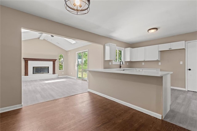 kitchen featuring kitchen peninsula, dark hardwood / wood-style flooring, a brick fireplace, white cabinets, and vaulted ceiling with beams