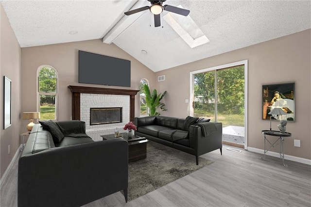 living room with a skylight, light hardwood / wood-style flooring, ceiling fan, a textured ceiling, and beamed ceiling