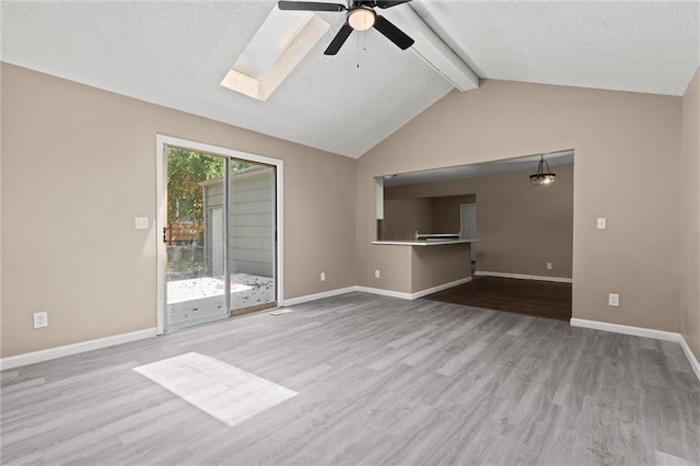 unfurnished living room featuring a textured ceiling, light hardwood / wood-style flooring, ceiling fan, and vaulted ceiling with skylight