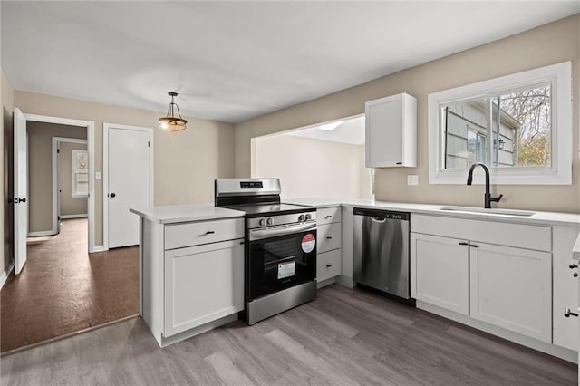 kitchen with white cabinetry, sink, kitchen peninsula, decorative light fixtures, and appliances with stainless steel finishes