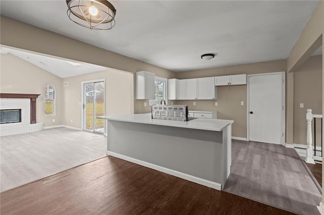 kitchen featuring a fireplace, white cabinetry, dark wood-type flooring, and vaulted ceiling