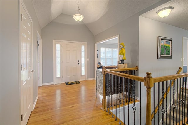 foyer entrance featuring lofted ceiling, a textured ceiling, and light hardwood / wood-style flooring