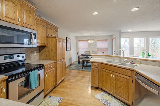 kitchen featuring sink, appliances with stainless steel finishes, pendant lighting, light hardwood / wood-style floors, and backsplash