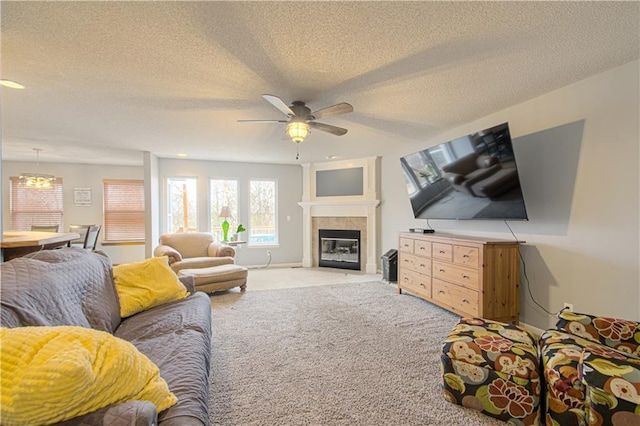 living room with light carpet, a ceiling fan, a tiled fireplace, a textured ceiling, and baseboards