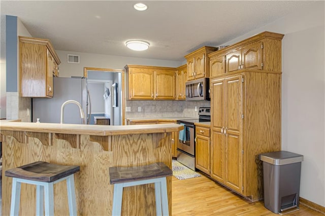 kitchen featuring visible vents, backsplash, a kitchen bar, a peninsula, and stainless steel appliances