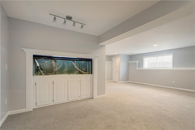 basement featuring baseboards, light carpet, and track lighting