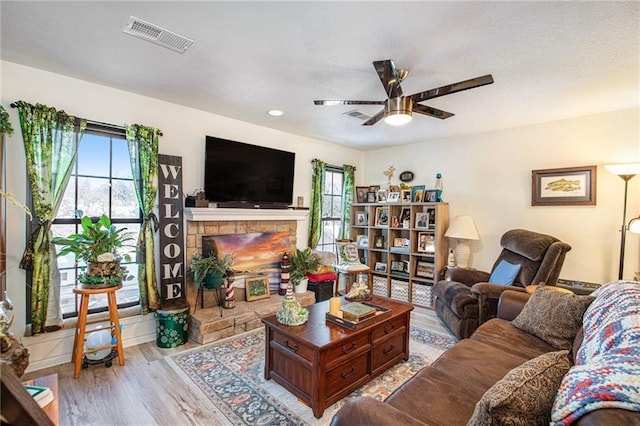 living room featuring a stone fireplace, ceiling fan, and light hardwood / wood-style floors