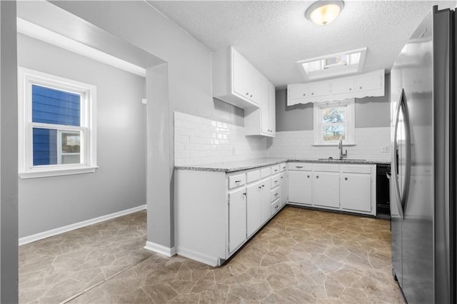 kitchen with sink, decorative backsplash, stainless steel fridge, a textured ceiling, and white cabinetry