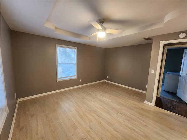 spare room featuring ceiling fan, light hardwood / wood-style floors, a raised ceiling, and washer / clothes dryer