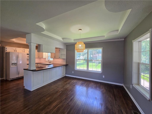 909 N Fulton St, Butler, MO 64730 - kitchen featuring white refrigerator with ice dispenser, a raised ceiling, healthy amount of natural light, and dark countertops