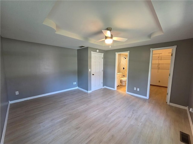 909 N Fulton St, Butler, MO 64730 - unfurnished bedroom featuring a raised ceiling, wood finished floors, a spacious closet, a closet, and a ceiling fan