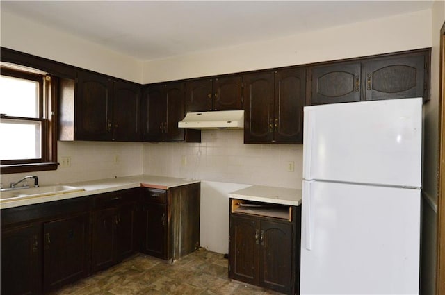 kitchen with dark brown cabinets, white fridge, decorative backsplash, and sink