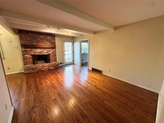 unfurnished living room with beam ceiling, hardwood / wood-style floors, and a brick fireplace