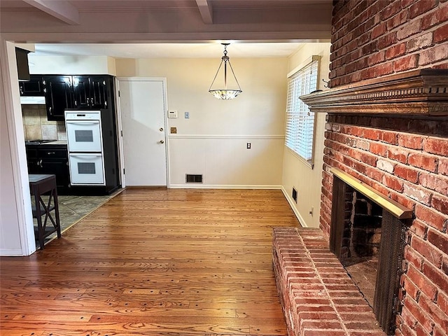 kitchen featuring beamed ceiling, white double oven, hardwood / wood-style flooring, and a fireplace