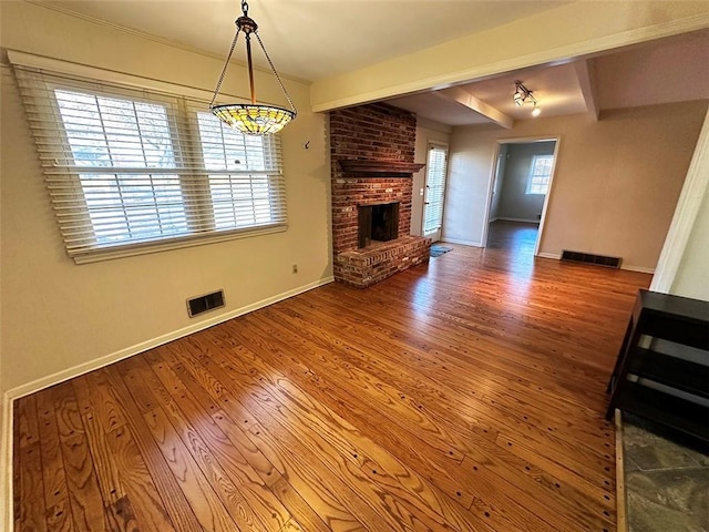 unfurnished living room with beam ceiling, wood-type flooring, a wealth of natural light, and a brick fireplace