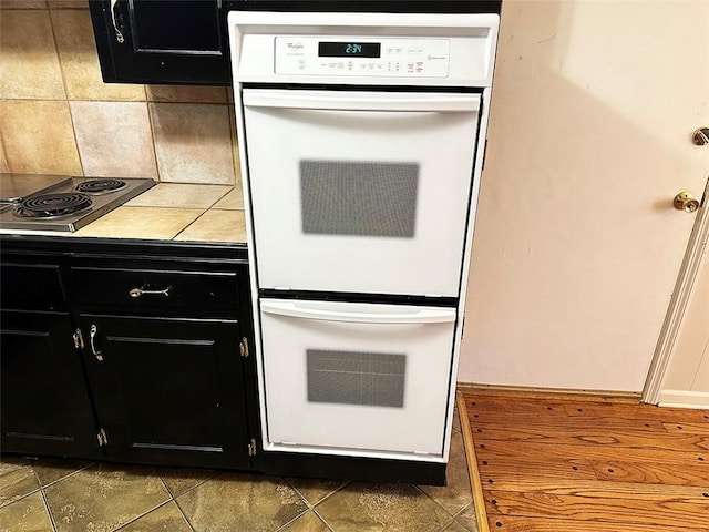 kitchen with double oven, stainless steel stovetop, tasteful backsplash, and dark tile patterned floors