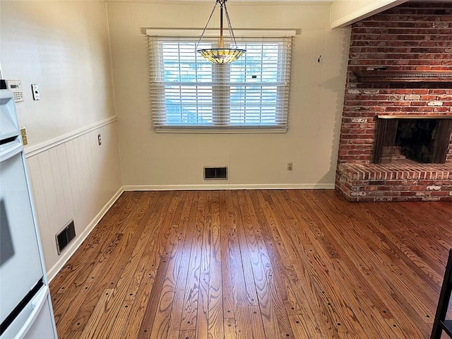 unfurnished dining area featuring hardwood / wood-style floors and a brick fireplace