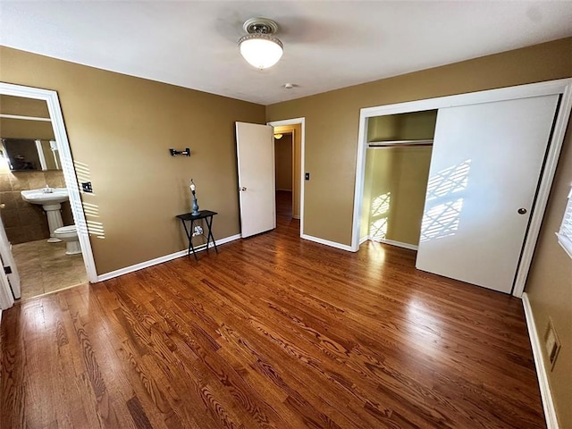 unfurnished bedroom with ensuite bathroom, a closet, and hardwood / wood-style flooring