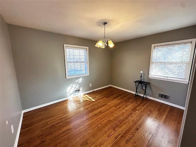 unfurnished room with dark hardwood / wood-style floors, a healthy amount of sunlight, and a notable chandelier