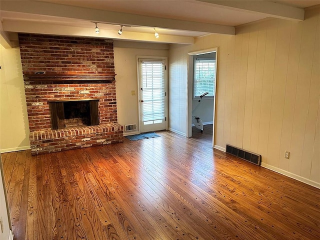 unfurnished living room with hardwood / wood-style floors, beam ceiling, wood walls, and a fireplace