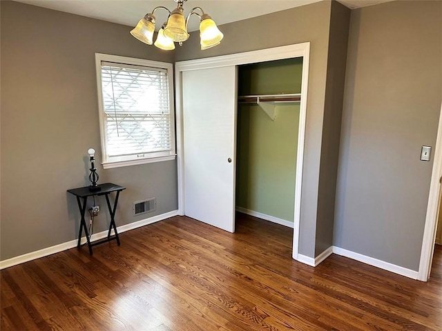 unfurnished bedroom featuring a closet, dark wood-type flooring, and a notable chandelier