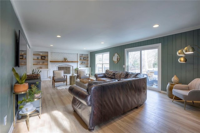 living room featuring built in shelves, crown molding, a brick fireplace, and light wood-type flooring