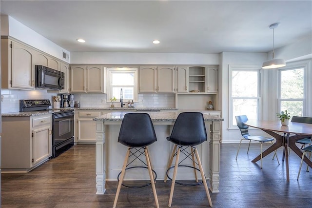 kitchen featuring backsplash, hanging light fixtures, a center island, black appliances, and light stone countertops