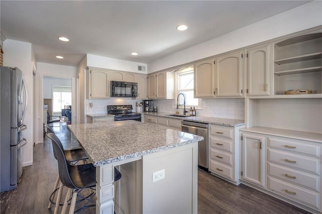 kitchen with sink, dark hardwood / wood-style flooring, a kitchen island, light stone countertops, and black appliances