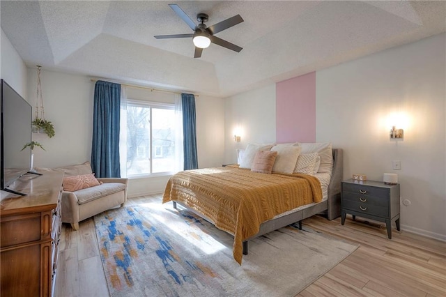 bedroom with ceiling fan, a tray ceiling, light hardwood / wood-style flooring, and a textured ceiling